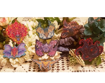 May include: A collection of intricately designed wooden ornaments in various shapes, including dragons and winged creatures. The ornaments feature vibrant colors like red, blue, purple, and gold. They are arranged on a bed of white and green flowers.
