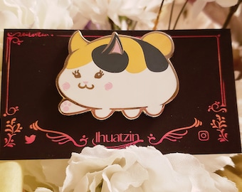 Puede incluir: Un pin de esmalte de color dorado con un gato de dibujos animados con orejas negras, marcas amarillas y negras y mejillas rosadas. El gato sonríe y tiene los ojos cerrados. El pin está sobre un fondo negro con diseños florales rosas y el texto "Ihuatzin".