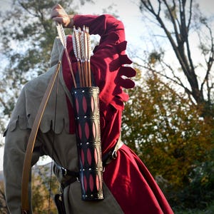 May include: A person wearing a red and grey tunic with a quiver of arrows strapped to their back. The quiver is made of black leather with pink accents and has a strap that goes over the shoulder.