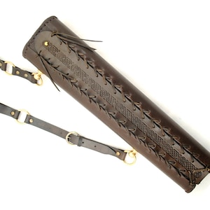 May include: A brown leather quiver with a Celtic knot design and a strap with brass buckles. The quiver is designed to hold arrows for archery.