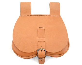 May include: A light brown leather pouch with a curved bottom and a flap closure secured by a metal buckle. The pouch has two loops at the top for attaching to a belt. The leather has a natural, textured appearance.