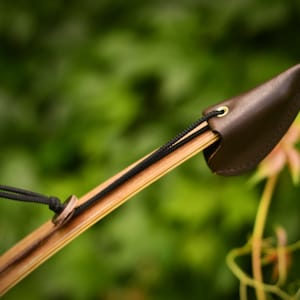 Könnte beinhalten: Nahaufnahme eines Holzbogens mit einer braunen Lederspitze. Die Spitze ist mit einer schwarzen Schnur und einem Messingring befestigt.