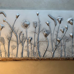 May include: A white rectangular wall art piece with a raised relief design of a field of wildflowers. The flowers are in shades of gray and white and are arranged in a random pattern. The piece is mounted on a wooden base.