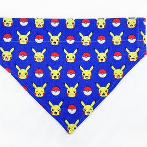 May include: Blue dog bandana featuring a repeating pattern of yellow Pikachu characters and red and white Poké Balls. The bandana is triangular in shape and made of fabric.