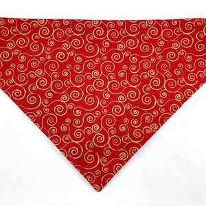 Puede incluir: Bandana roja para perro con un patrón de espiral dorado.