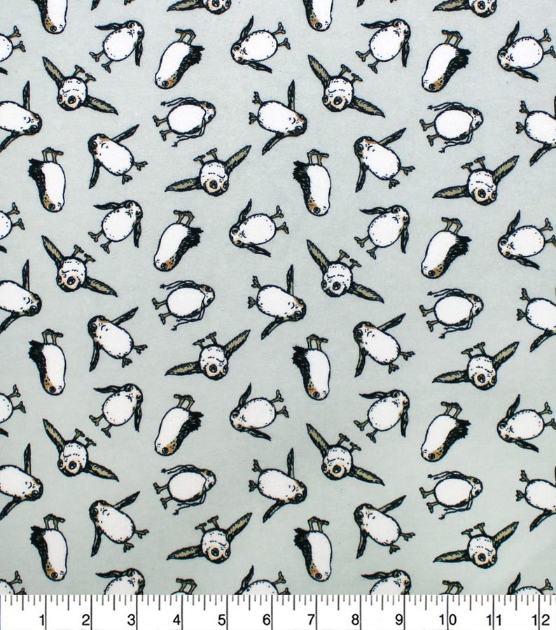 May include: Light blue fabric with a repeating pattern of cartoon penguins. The penguins are white with black and brown accents, and are depicted in various poses. The fabric has a ruler along the bottom edge, with measurements in inches.