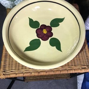 May include: A large, cream-colored ceramic bowl with a dark brown floral design. The bowl has a black rim and a green and brown floral pattern.