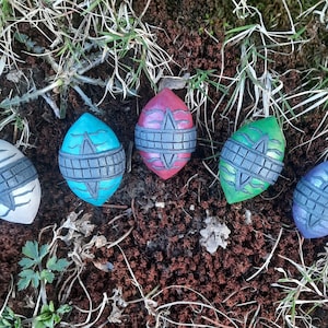 Puede incluir: Seis adornos de cerámica en forma de huevo con un diseño geométrico. Los adornos están pintados en varios colores, incluyendo blanco, azul, verde, rojo y morado.