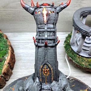 May include: A detailed, gray fantasy tower sculpture with red accents, including horns and spikes. The tower has a glowing center and sits on a wooden base with orange markings. The tower's door has a golden symbol.