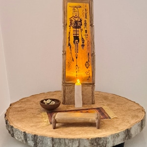 May include: A wooden base with a lit candle, a small bowl, and a scroll. A wooden frame with a lit image of a figure with symbols and text is on top of the base.