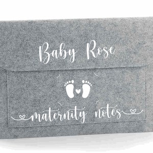 May include: Grey felt folder with a white design. The design includes the text "Baby Rose" and "maternity notes" with a pair of footprints and a heart.