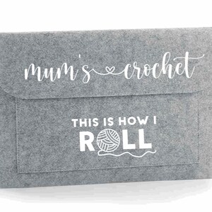 K&ouml;nnte beinhalten: Graue Filztasche mit wei&szlig;em Design, auf dem "mum's crochet" und "This is how I ROLL" mit einer Wollkn&auml;uelgrafik steht.