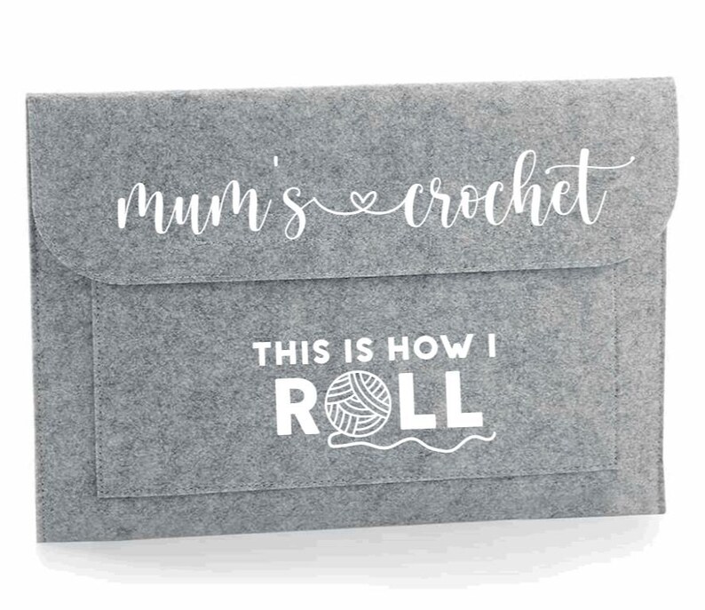 K&ouml;nnte beinhalten: Graue Filztasche mit wei&szlig;em Design, auf dem "mum's crochet" und "This is how I ROLL" mit einer Wollkn&auml;uelgrafik steht.
