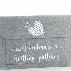 May include: Grey felt storage envelope with a white heart-shaped yarn ball and knitting needles design. The text "Grandma's knitting patterns" is printed on the front.