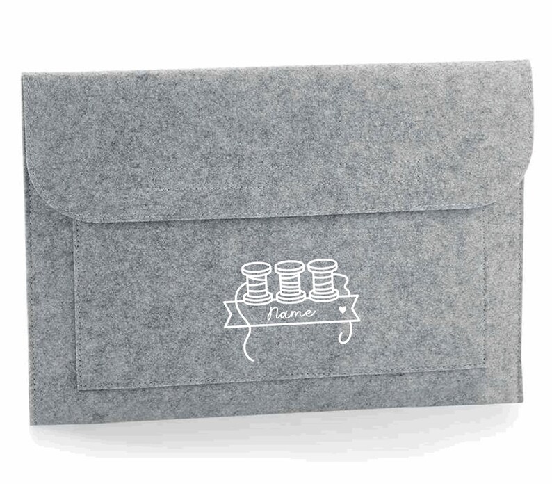 K&ouml;nnte beinhalten: Graue Filz-Laptoptasche mit einem wei&szlig;en Design aus drei Garnrollen und einem Banner mit dem Wort "name".