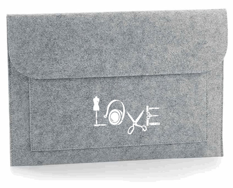 K&ouml;nnte beinhalten: Graue Filz-Laptoptasche mit einem wei&szlig;en Design aus N&auml;hmaschine, Kopfh&ouml;rern, Schere und Faden. Das Design ist so angeordnet, dass es das Wort "LOVE" buchstabiert.