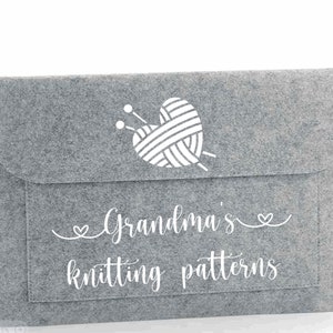 May include: Gray felt storage envelope with a white heart-shaped yarn ball and knitting needles design. The text "Grandma's knitting patterns" is printed on the front.