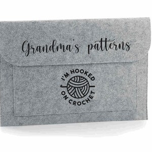 K&ouml;nnte beinhalten: Graue Filz-Aufbewahrungsh&uuml;lle mit einer schwarzen Aufschrift "Grandma's patterns" und einer schwarz-wei&szlig;en Grafik einer Wollkn&auml;uel mit dem Text "I'm hooked on crochet".