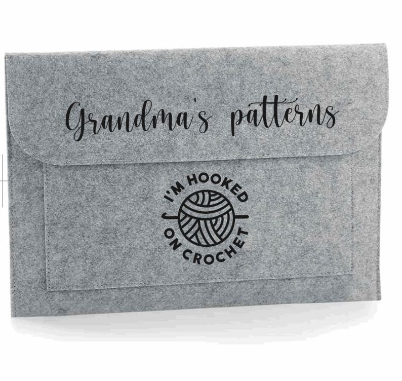 K&ouml;nnte beinhalten: Graue Filz-Aufbewahrungsh&uuml;lle mit einer schwarzen Aufschrift "Grandma's patterns" und einer schwarz-wei&szlig;en Grafik einer Wollkn&auml;uel mit dem Text "I'm hooked on crochet".
