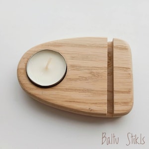 Op de afbeelding: Een houten kaarsenhouder met een kleine, ronde inkeping voor een theelichtje. De houder heeft een rechthoekige gleuf aan de zijkant, waarschijnlijk voor een telefoon of een ander apparaat. De houder is gemaakt van licht hout met een natuurlijke houtnerf.