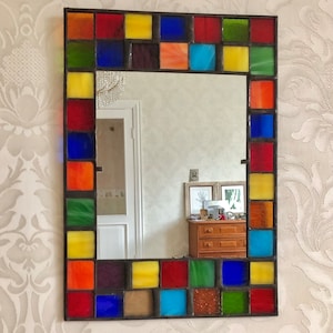 May include: A square mirror with a colorful stained glass frame. The frame is made up of small squares of red, yellow, blue, green, and orange glass.