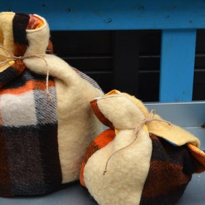 Op de afbeelding: Twee handgemaakte theemutsen. De grotere muts is lichtgeel met een ruitpatroon van oranje, zwart en wit. De kleinere muts heeft een vergelijkbaar ontwerp. Beide zijn vastgebonden met touw.