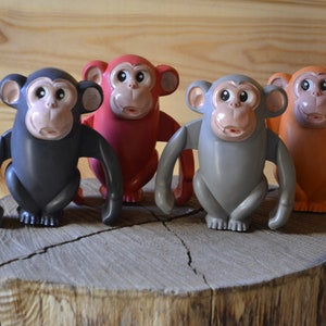 May include: Four toy monkeys in different colors: black, red, gray, and orange. The monkeys are all sitting on a wooden stump.