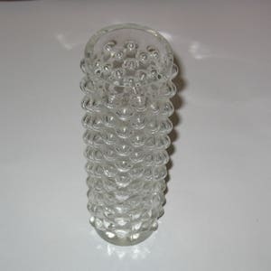 May include: A clear glass vase with a textured, bubble-like design. The vase is cylindrical and has a rounded top.