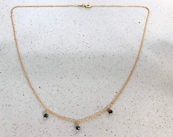 Op de afbeelding: Een gouden ketting met drie zwarte kralen die eraan hangen.
