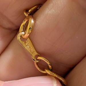 May include: A gold-toned metal chain necklace featuring a flat, triangular-shaped clasp component. The clasp is engraved with the text "&copy;DISNEY" and connects to a series of oval-shaped links that form the main body of the jewelry piece.