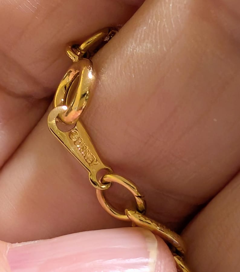 May include: A gold-toned metal chain necklace featuring a flat, triangular-shaped clasp component. The clasp is engraved with the text "&copy;DISNEY" and connects to a series of oval-shaped links that form the main body of the jewelry piece.