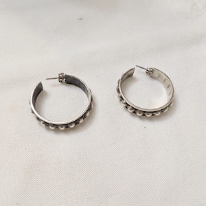 May include: A pair of silver hoop earrings featuring a row of small, raised spherical beads along the outer edge. The earrings have a polished metallic finish and include a standard post-back closure mechanism for secure attachment to the earlobe.