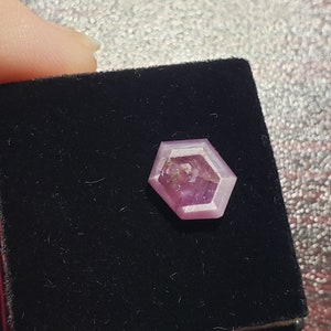 May include: A hexagonal shaped, faceted, pink gemstone in a black velvet box.