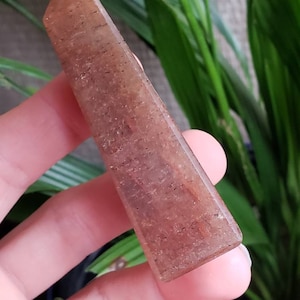 May include: A light brown, translucent crystal point with a rough, textured surface. The crystal is held in a hand.