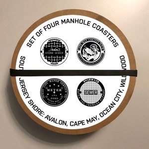 May include: A set of four round brown coasters with white manhole covers printed on them. The coasters feature the text "Set of Four Manhole Coasters" and the names of the towns "Avalon, Cape May, Ocean City, Wildwood".