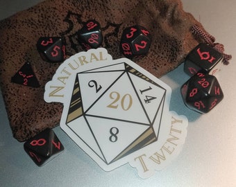 May include: A black and white sticker with a gold design of a twenty-sided die. The sticker says "Natural Twenty". There are several black dice with red numbers on a brown leather bag.