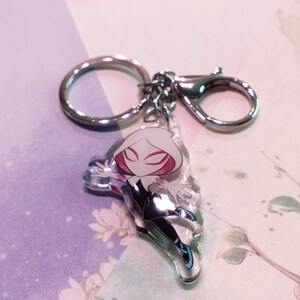 May include: A silver keychain with a clear acrylic charm featuring a cartoon character. The character is a white and black spider-person with a red mask.