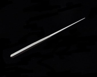 Peut inclure: Un outil en métal argenté avec une pointe pointue, probablement utilisé pour l'artisanat ou la fabrication de bijoux.