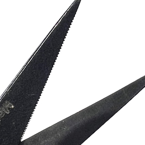 Pode incluir: Close-up de tesoura de metal preto com uma lâmina serrilhada. A tesoura está sobre um fundo branco, destacando as pontas afiadas e a superfície texturizada do metal.