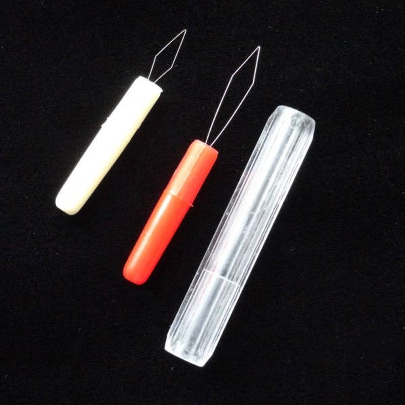 May include: Three plastic threaders for threading needles. The threaders are white, red, and clear. The threaders have a needle at the end.