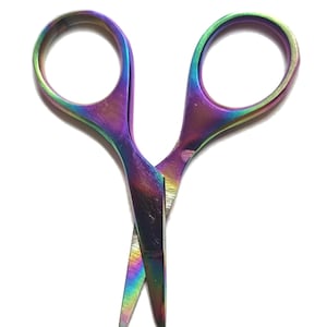 Può includere: Un paio di forbici piccole caratterizzate da una vibrante finitura iridescente color arcobaleno su tutta la superficie metallica. Le forbici presentano due anelli circolari e lame affilate e appuntite posizionate in modo incrociato e leggermente aperto.