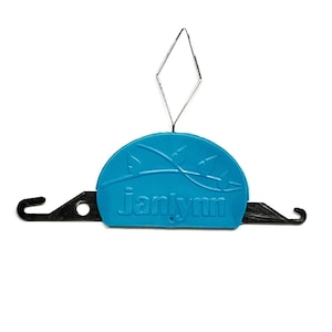May include: A blue Janlynn brand needle threader with a diamond-shaped wire and black hooks on each side. The threader has the brand name printed in white.