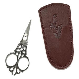 May include: A pair of silver decorative scissors with a floral design, in a burgundy leather case with a floral design.
