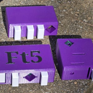May include: Three purple rectangular objects with white and green accents. One object has the text "Ft5" on it. Each object has a diamond-shaped indentation and white rectangular protrusions.