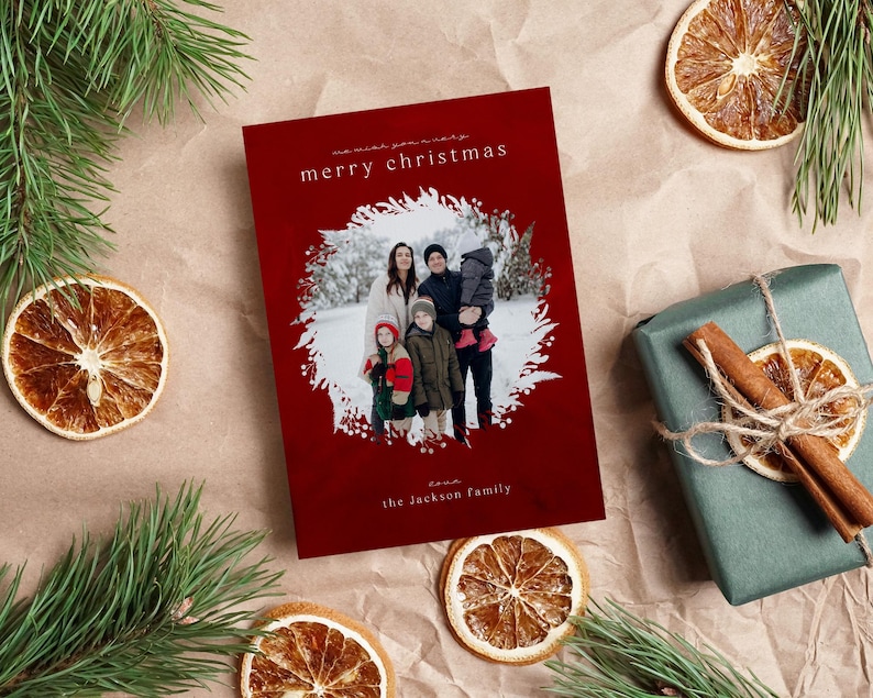May include: A rectangular Christmas greeting card with a deep red background featuring a central circular photo of a family of four in a snowy setting. The card includes the white text merry christmas and the jackson family in a minimalist font.