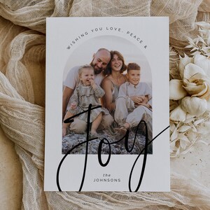 Może przedstawiać: Biała kartka ze zdjęciem rodzinnym, z tekstem "Wishing You Love, Peace & Joy" w łuku nad zdjęciem. Słowo "Joy" jest napisane dużą, kursywą na dole, z napisem "the Johnsons" poniżej.