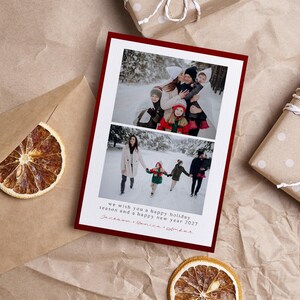 May include: A rectangular holiday greeting card with a dark red border featuring two stacked photographs of a family in a snowy landscape. The card includes the printed text: we wish you a happy holiday season and a happy new year 2027.