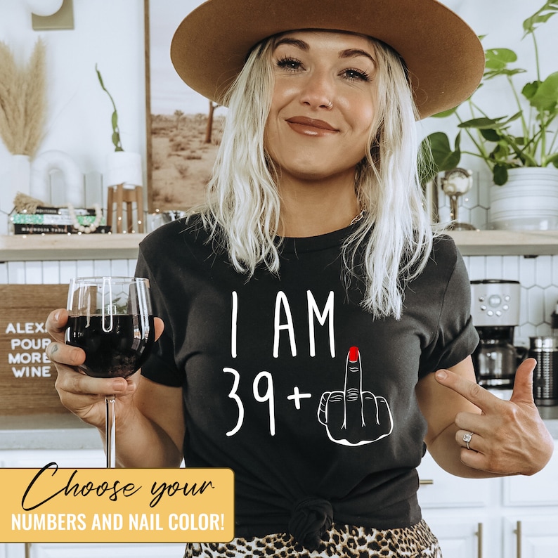 Pode incluir: Camiseta preta com texto branco que diz "I AM 39+" e uma m&atilde;o preta com uma unha vermelha fazendo o dedo do meio. Escolha seus n&uacute;meros e a cor da unha!