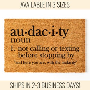 May include: A rectangular doormat with a light brown, textured surface. The word "audacity" is printed in black, along with a definition. The definition reads "1. not calling or texting before stopping by" and "and here you are, with the audacity."