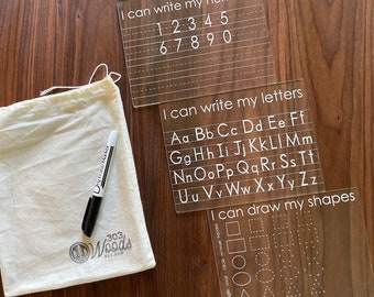May include: Three clear acrylic learning boards with white text. The first board has the numbers 1-9 written on it with the text "I can write my numbers". The second board has the alphabet written on it with the text "I can write my letters". The third board has various shapes outlined with the text "I can draw my shapes".